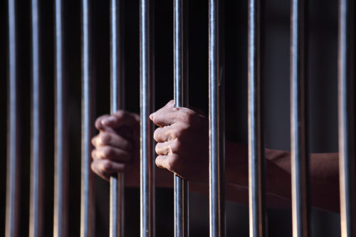 jail person behind bars holding on to bars